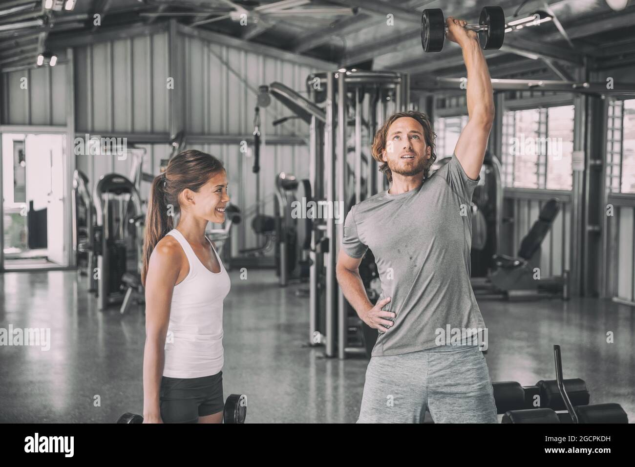 Fitness gym entraîneur personnel entraîneur d'entraînement asiatique femme avec des poids libres dumbbbell bicep boucles d'entraînement parler avoir plaisir partenaire d'exercice. Poser l'homme Banque D'Images
