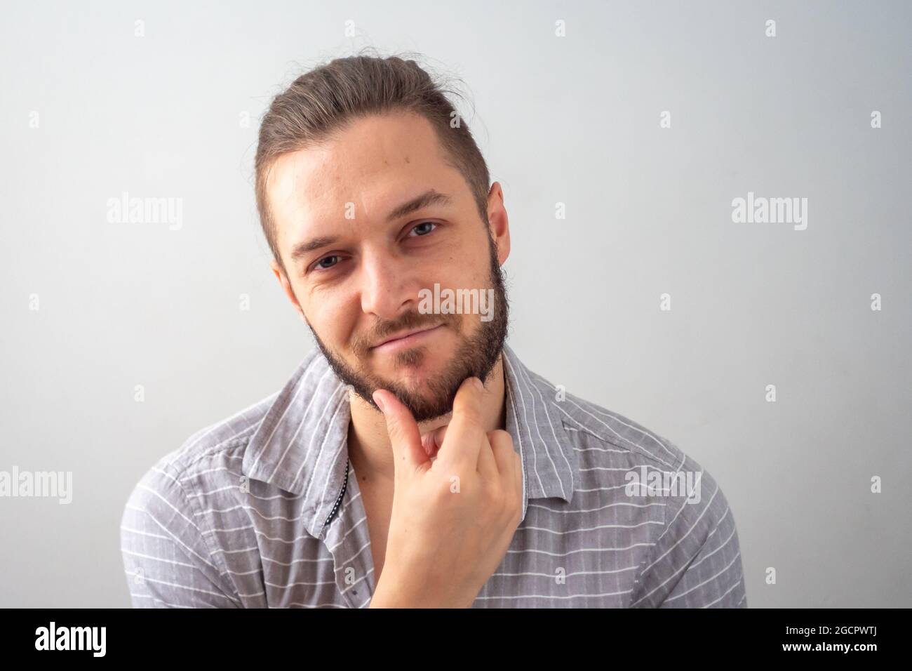 Un jeune homme de race blanche se fait un plaisir de gratter son maillot Chin in Grey contre fond blanc Banque D'Images