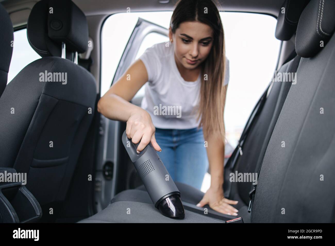 Femme passant l'aspirateur dans son siège arrière dans sa voiture dans le garage à la maison. Femme utilisant un aspirateur portable pour enlever la poussière et la saleté. Nettoyage de l'intérieur de la voiture Banque D'Images