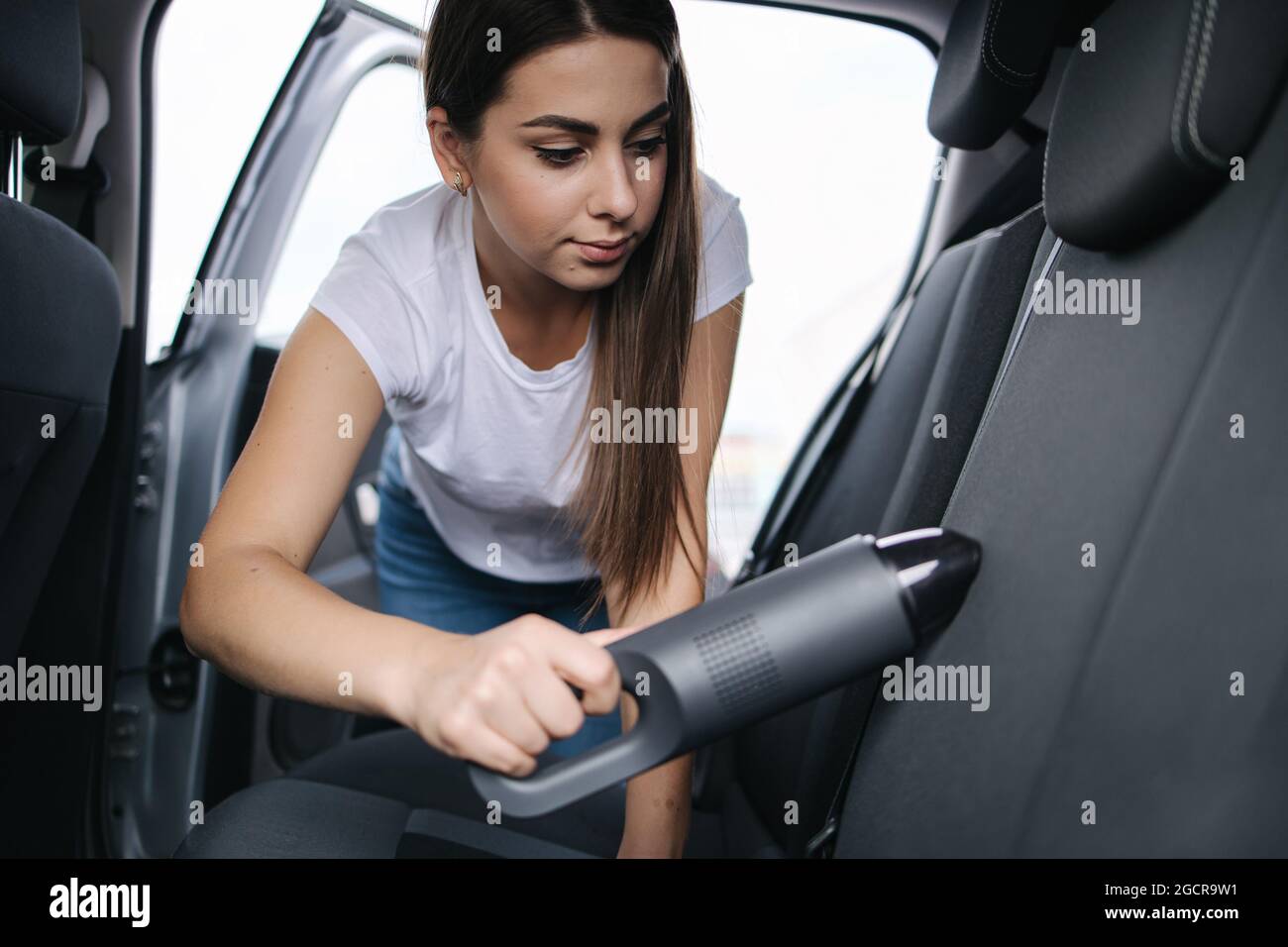 Jeune femme attrayante utilisant un aspirateur portable dans sa voiture.  Femme passant l'aspirateur de sa voiture dans le garage à la maison.  Nettoyage de l'intérieur de la voiture Photo Stock - Alamy