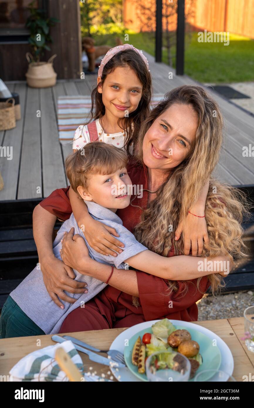 Les enfants gaies et leur jolie mère dînant près de leur maison de campagne Banque D'Images