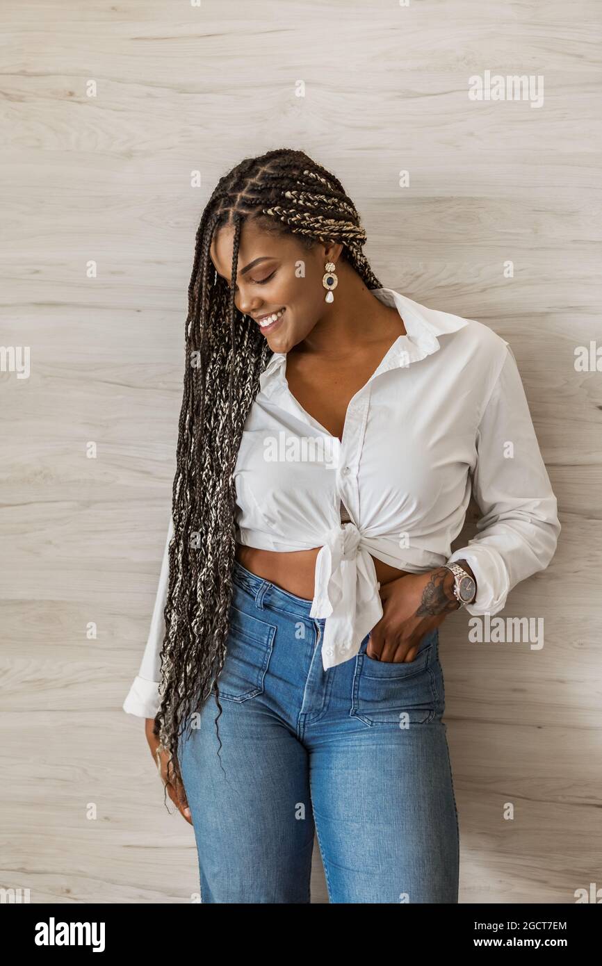 Portrait d'une femme adulte afro-américaine joyeuse debout avec son bras sur son corps et regardant vers le bas d'un côté. Femme adulte avec noir et jaune Banque D'Images