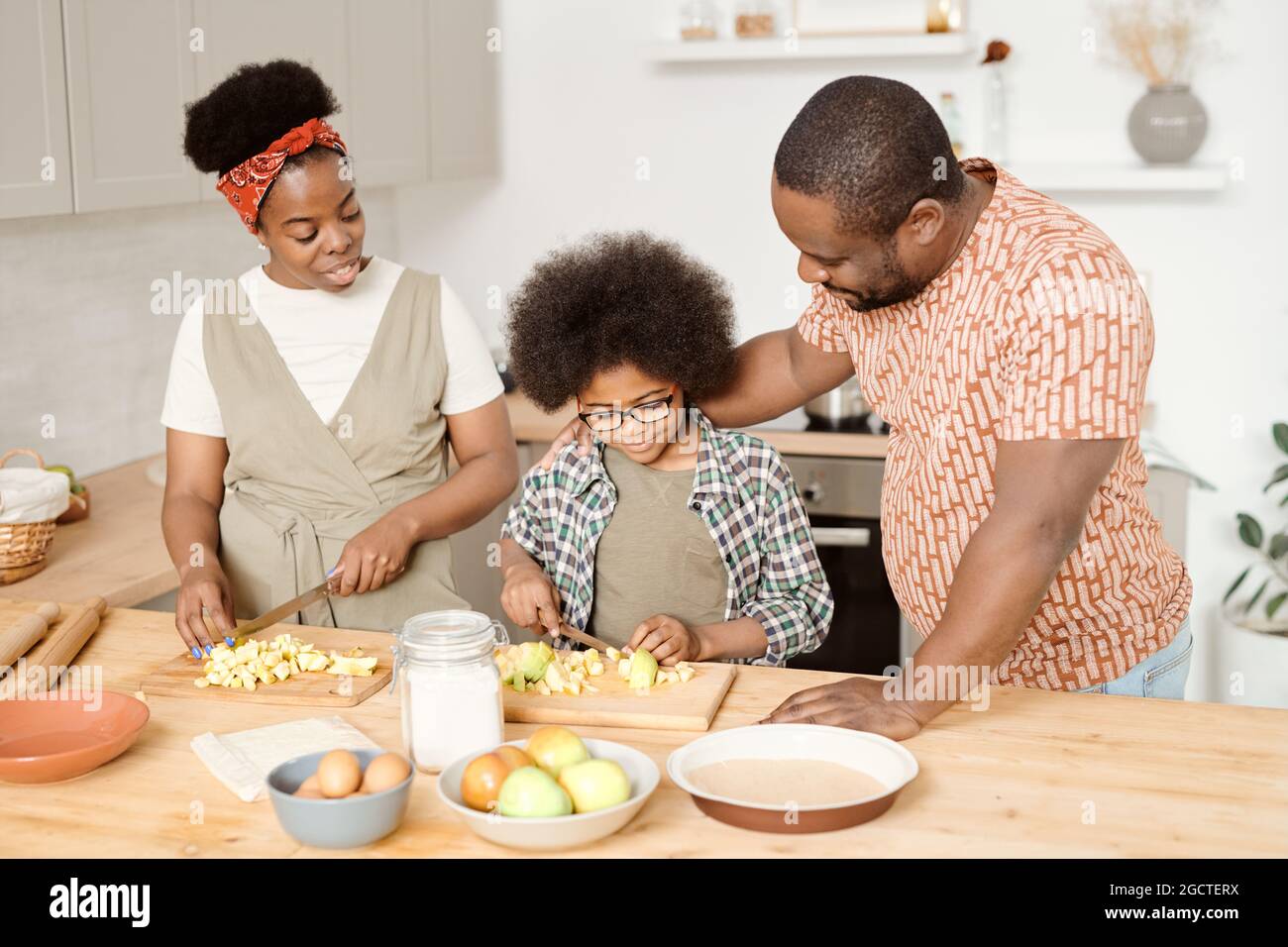 Jeune famille africaine de trois personnes préparant le petit déjeuner à table de cuisine Banque D'Images