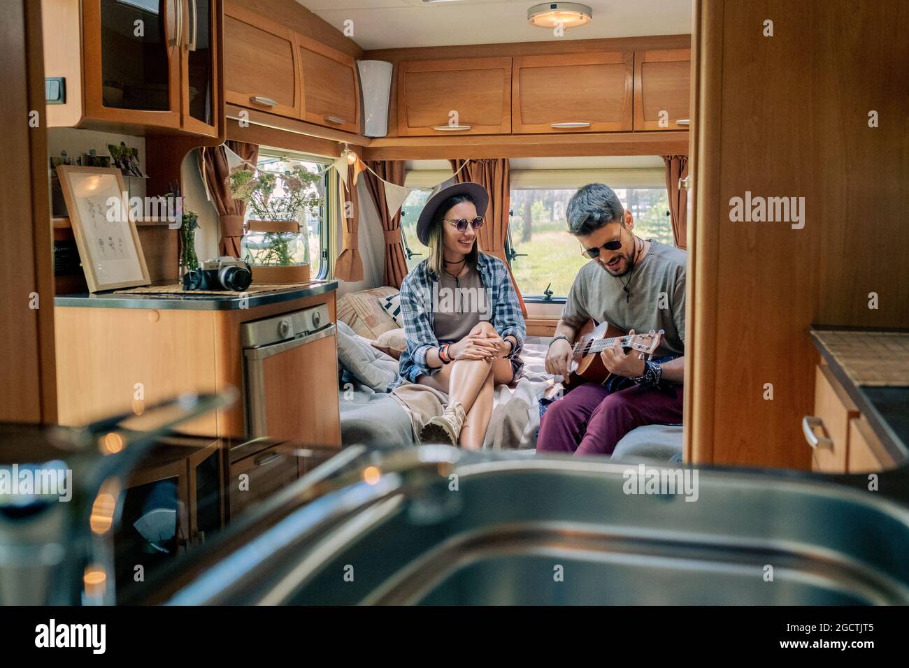 Guy en lunettes de soleil jouant de la guitare et chantant pour sa petite amie à l'intérieur de la maison mobile Banque D'Images