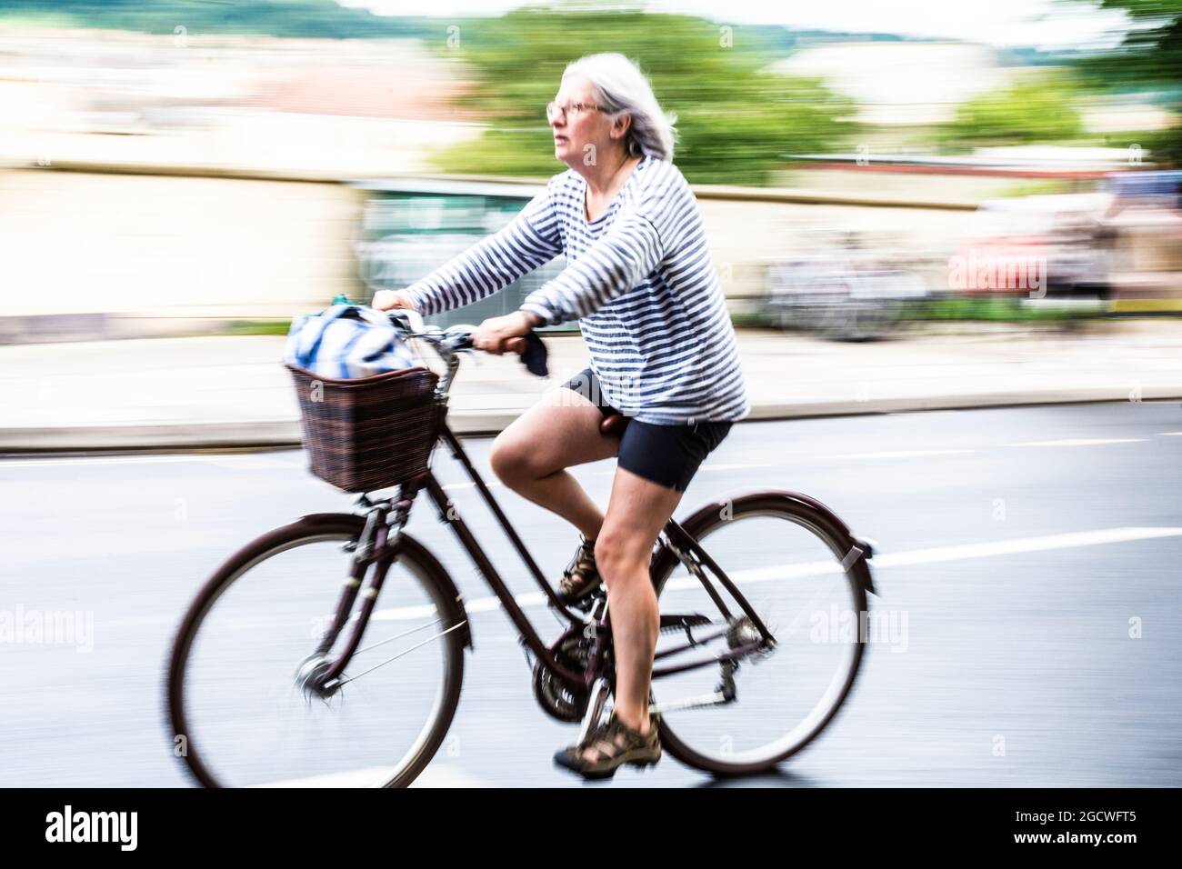 Femme d'âge moyen ou senior à vélo avec flou de vitesse. Bath Spa, Somerset, Royaume-Uni Banque D'Images