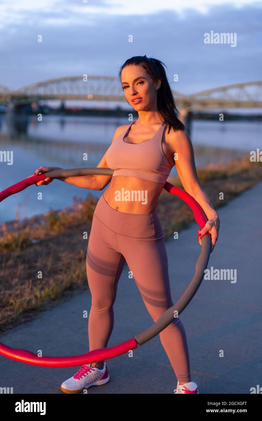 Jeune femme sportive tenant le hula hoop sur la rive pendant le coucher du soleil Banque D'Images