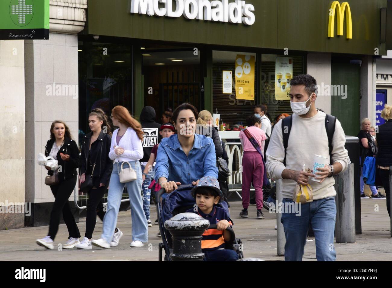 Manchester, Royaume-Uni, 10 août 2021. Une femme pousse un bébé avec un enfant à côté d'un homme portant un masque, pour aider à prévenir la propagation du virus Covid-19, à Manchester, au Royaume-Uni. Les taux d'infection par Covid-19 ou coronavirus chutent à Manchester, mais augmentent dans trois autres quartiers de Manchester : Stockport, Bury et Trafford, selon les dernières données de public Health England. Crédit : Terry Waller/Alay Live News Banque D'Images