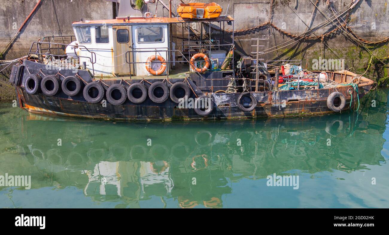 Old Tug Boat attaché le long du mur du port. Banque D'Images