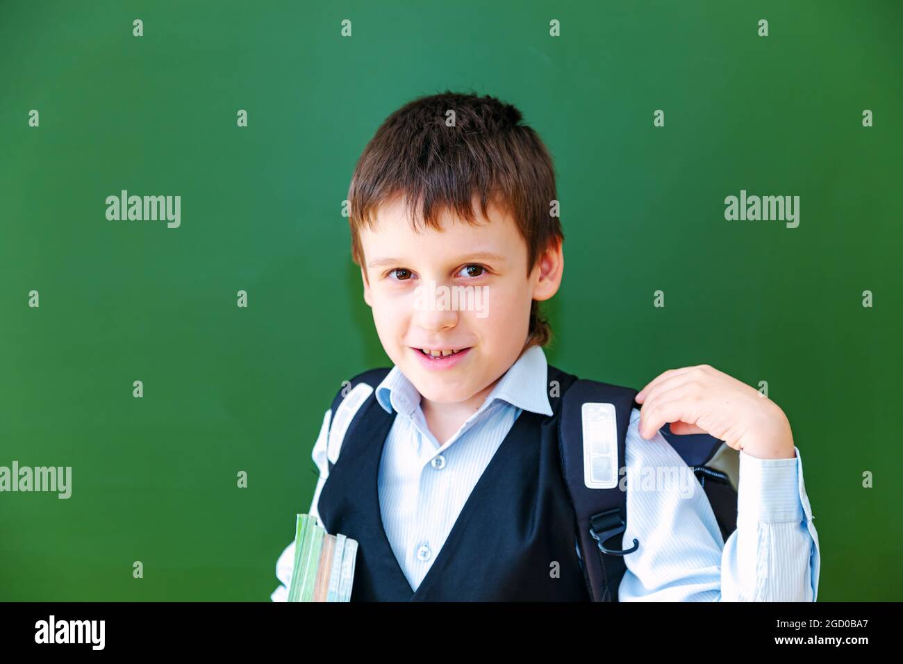 Drôle d'écolier grimaces près de la commission scolaire verte dans la salle de classe. Enfant de l'école primaire avec sac et livres. Retour à l'école. Banque D'Images