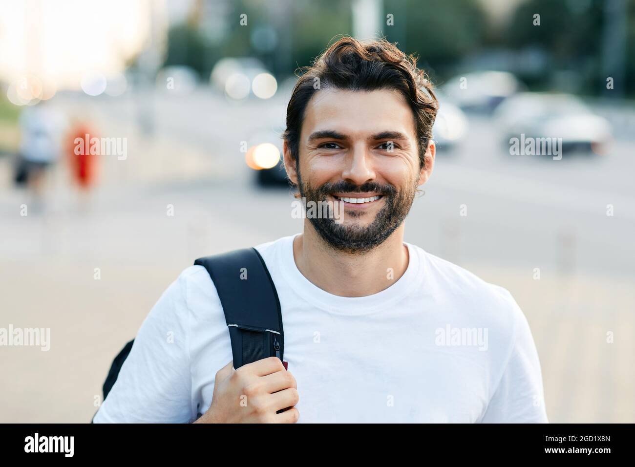 Portrait d'un bel homme avec un sourire blanc et crasseux sur une rue de ville tenant un sac à dos Banque D'Images