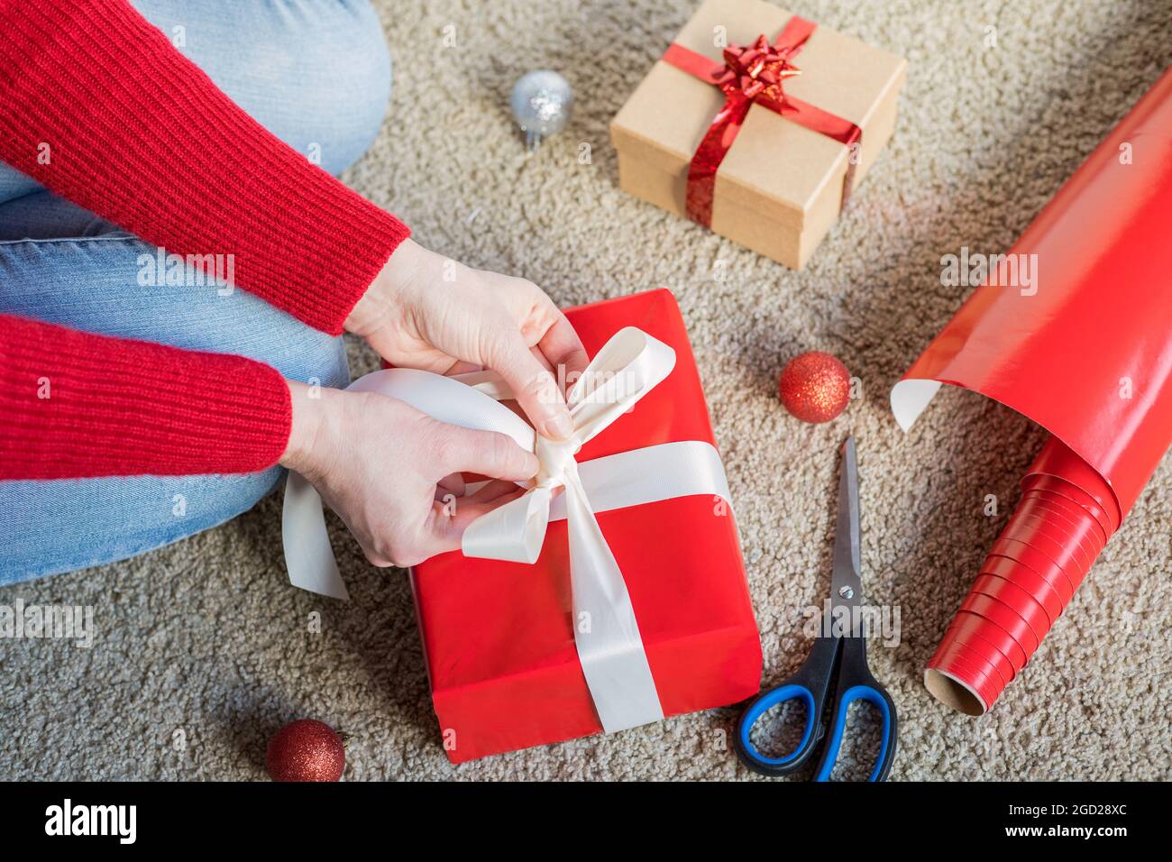 Préparation du papier cadeau des fêtes de Noël, papier d'emballage rouge et  boîtes-cadeaux. Femme préparant des cadeaux à la maison. Femme assise sur  le sol, cadeau d'emballage b Photo Stock - Alamy