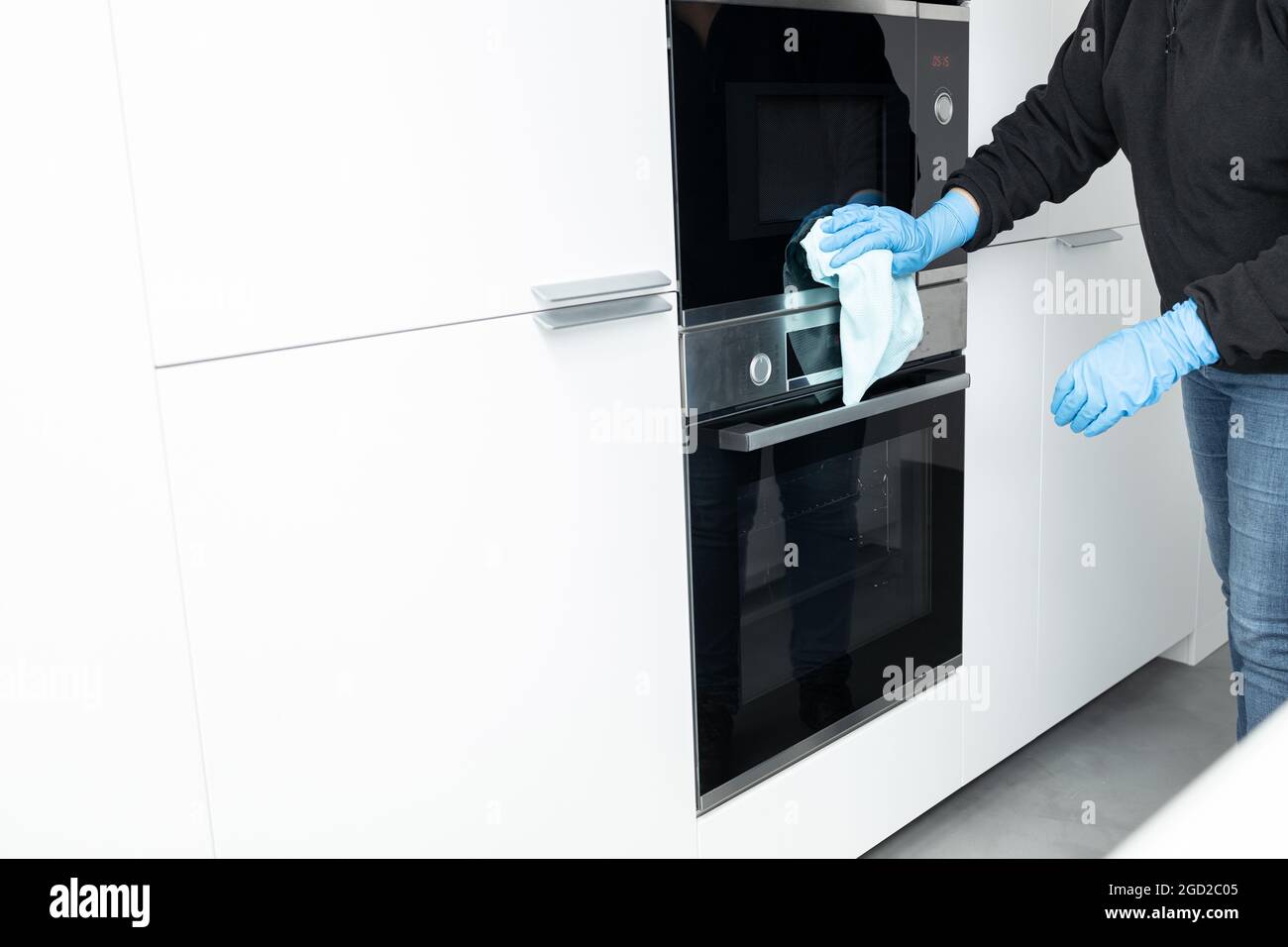 Femme nettoyant un appareil moderne en acier inoxydable avec un chiffon d'une cuisine minimaliste Banque D'Images