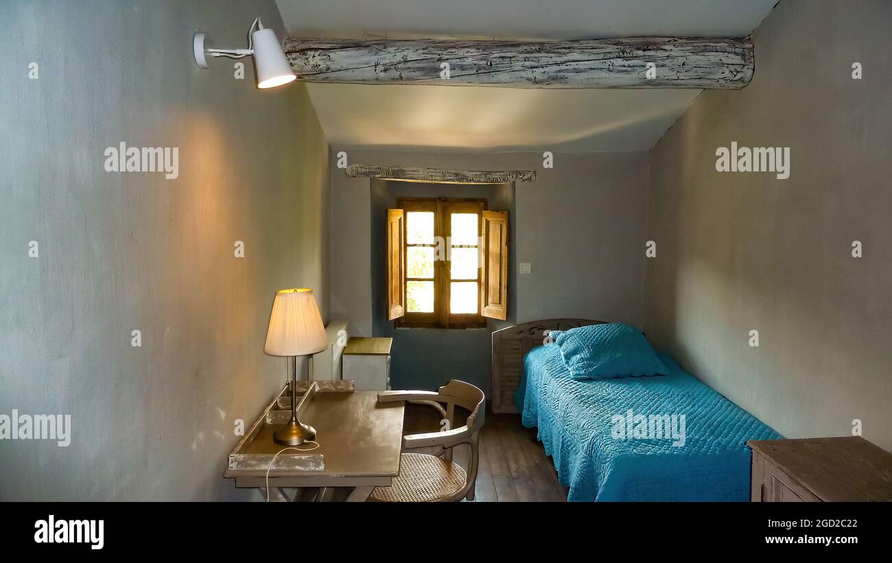 Grimod, France - juin 9. 2021: Vue dans une petite chambre à coucher avec table, lit couverture bleue et lumière naturelle lumineuse de la fenêtre Banque D'Images