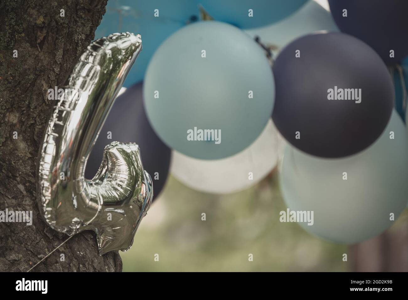 ballon d'argent numéro quatre attaché à un arbre avec une corde et dans le fond encore habituellement ballons en bleu, gris et blanc comme décor de fête d'enfants Banque D'Images