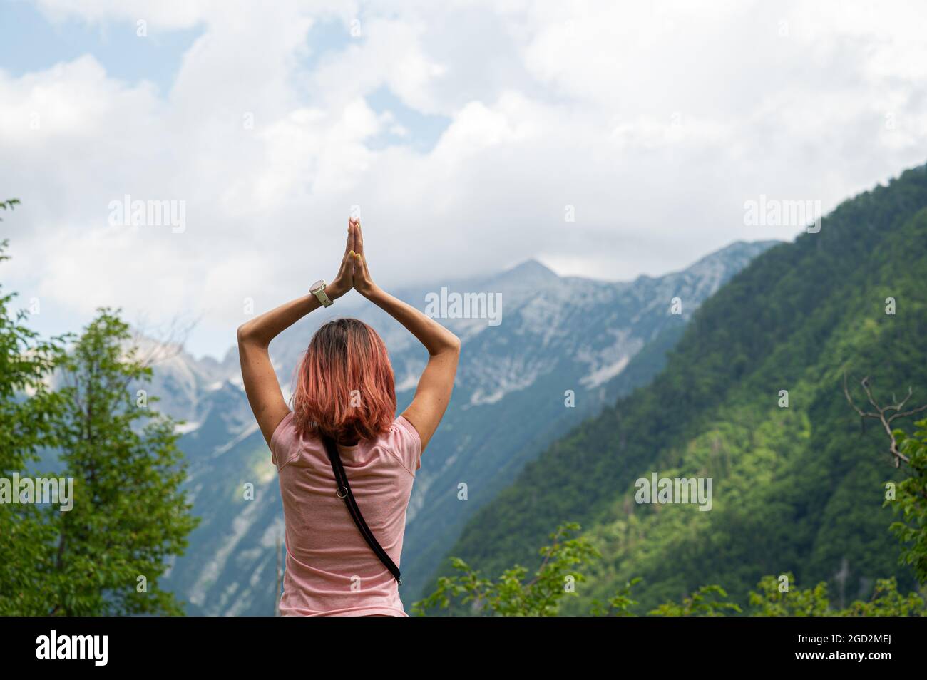 Vue de derrière une jeune femme debout dans une belle nature avec ses mains jointes au-dessus de sa tête dans une position de prière. Banque D'Images
