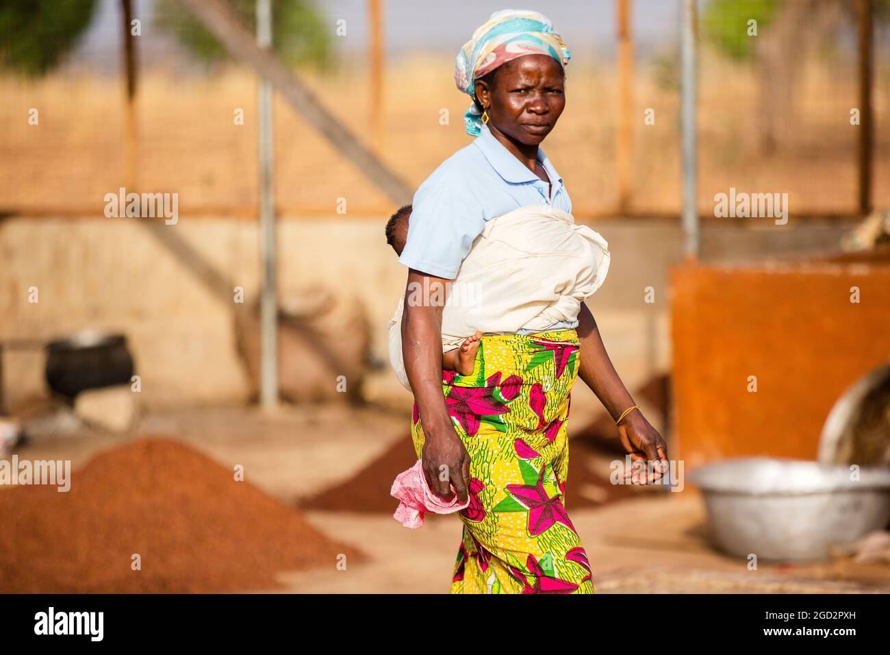 Une femme de village d'Afrique de l'Ouest avec un bébé marchant vers la droite dans un petit village africain ca. 21 février 2018 Banque D'Images