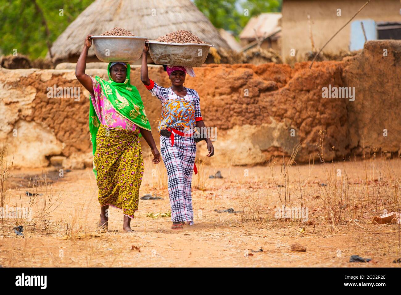Ces deux femmes de village d'Afrique de l'Ouest dans la robe traditionnelle colorée marcher avec de grands bols sur leur tête ca. 21 février 2018 Banque D'Images