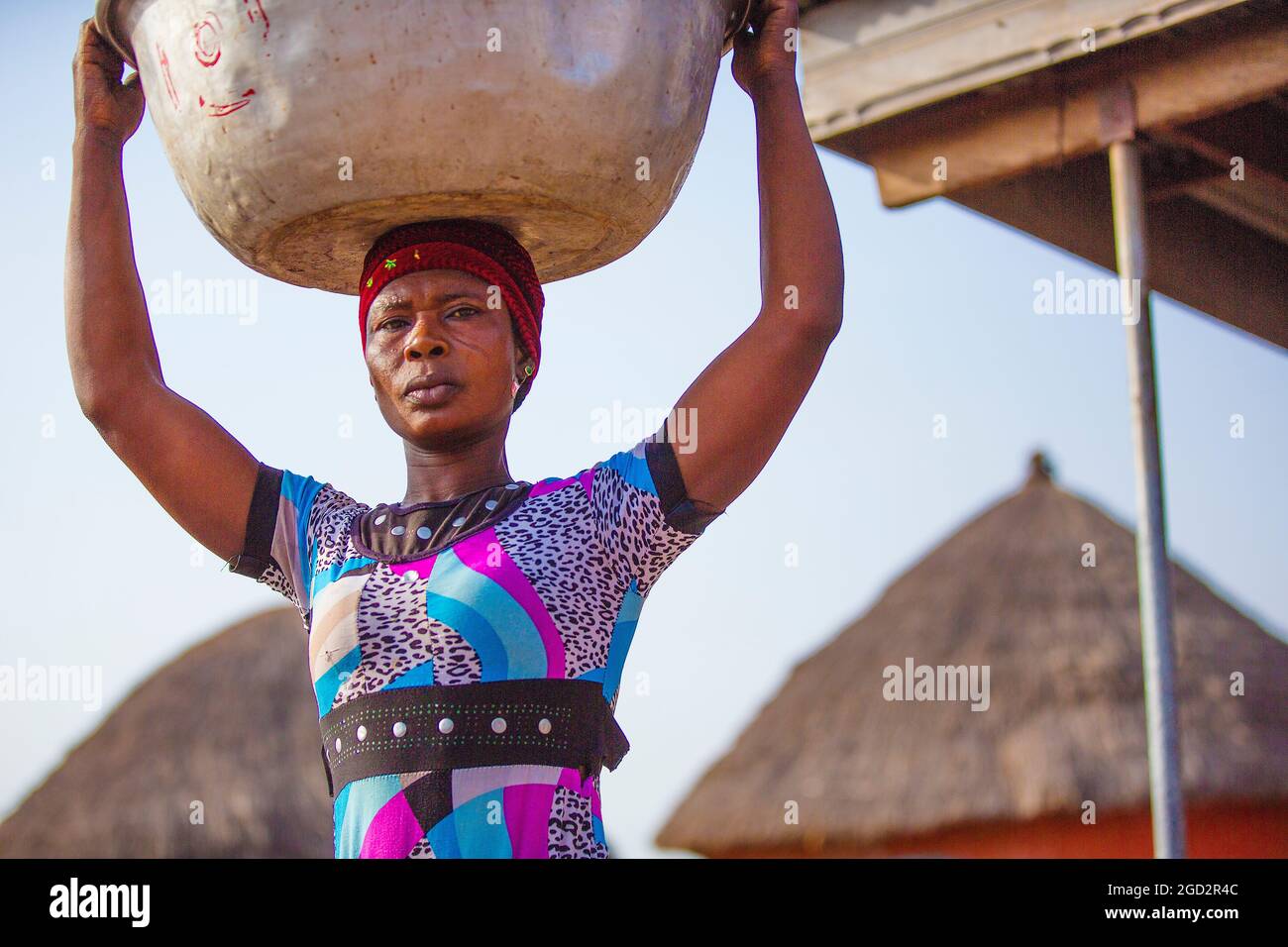 Une femme de village d'Afrique de l'Ouest portant une robe colorée portant un grand bol sur sa tête ca. 21 février 2018 Banque D'Images