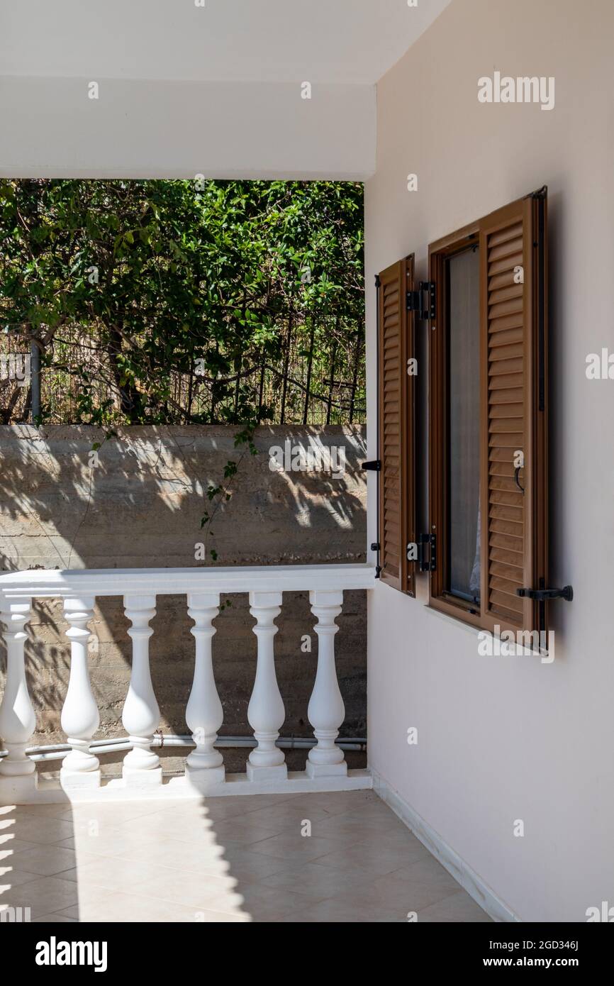 Terrasse blanche d'architecture grecque classique avec balusters et fenêtre avec volets. Vue sur la verdure dans l'ombre. L'été dans la maison de campagne près d'Ath Banque D'Images