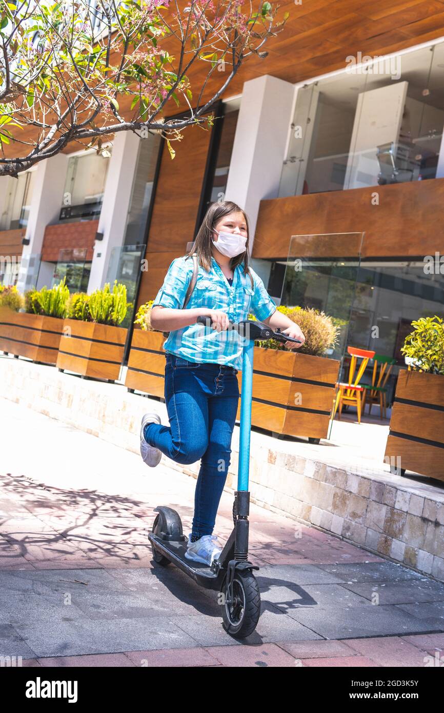 photo verticale d'une fille avec un masque sur son chemin à l'école sur un scooter électrique. Retour à l'école Banque D'Images