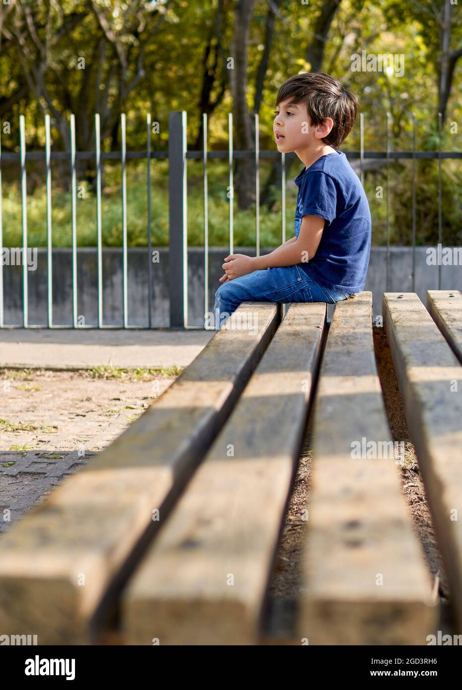 latino garçon assis dans le profil attendant sur un banc carré. vertical Banque D'Images