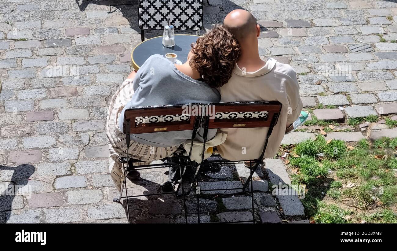 Un couple assis à la table basse à l'extérieur de la rue, deux chaises à côté de l'autre femme avec sa tête sur l'épaule de l'homme, affectueux. Banque D'Images