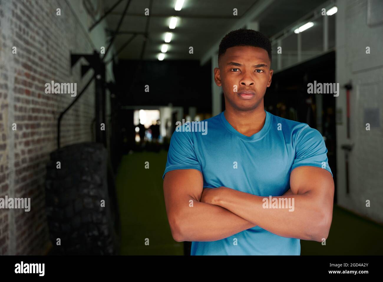 Homme afro-américain debout avec des armes croisées dans la salle de sport. Entraîneur personnel masculin regardant intensément la caméra. Photo de haute qualité Banque D'Images