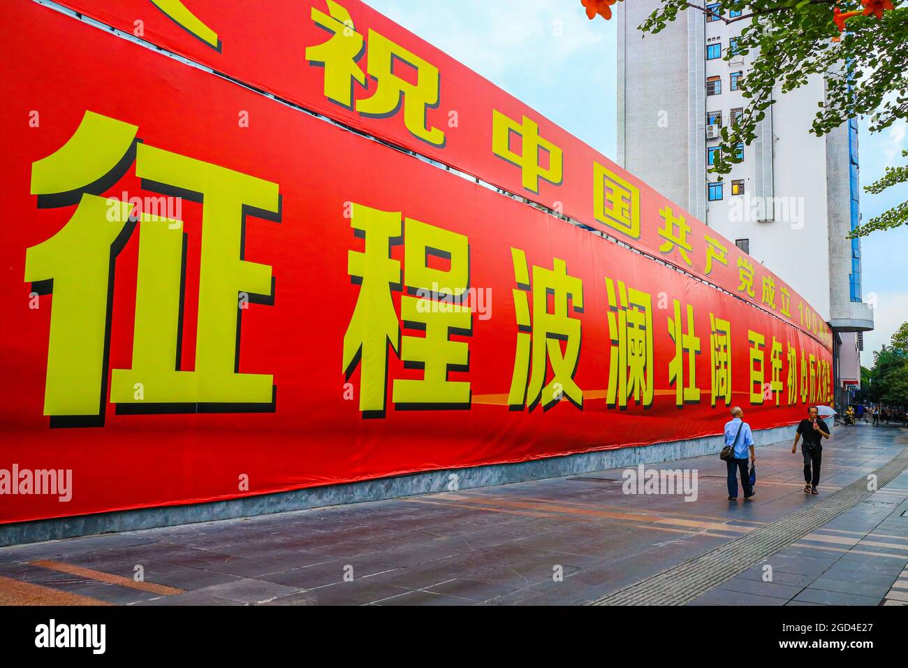 Les gens marchent devant une immense bannière commémorant le 100e anniversaire de la fondation du Parti communiste de Chine. Une bannière géante célébrant le 100e anniversaire de la fondation du Parti communiste de Chine est exposée sur l'avenue principale de Guilin, en Chine Banque D'Images