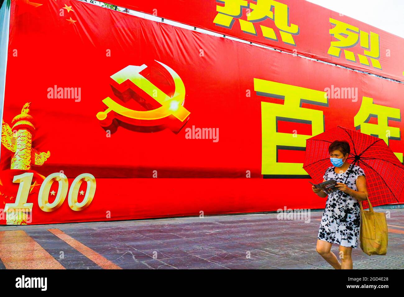 Une femme passe devant une immense bannière commémorant le 100e anniversaire de la fondation du Parti communiste chinois. Une bannière géante célébrant le 100e anniversaire de la fondation du Parti communiste de Chine est exposée sur l'avenue principale de Guilin, en Chine Banque D'Images