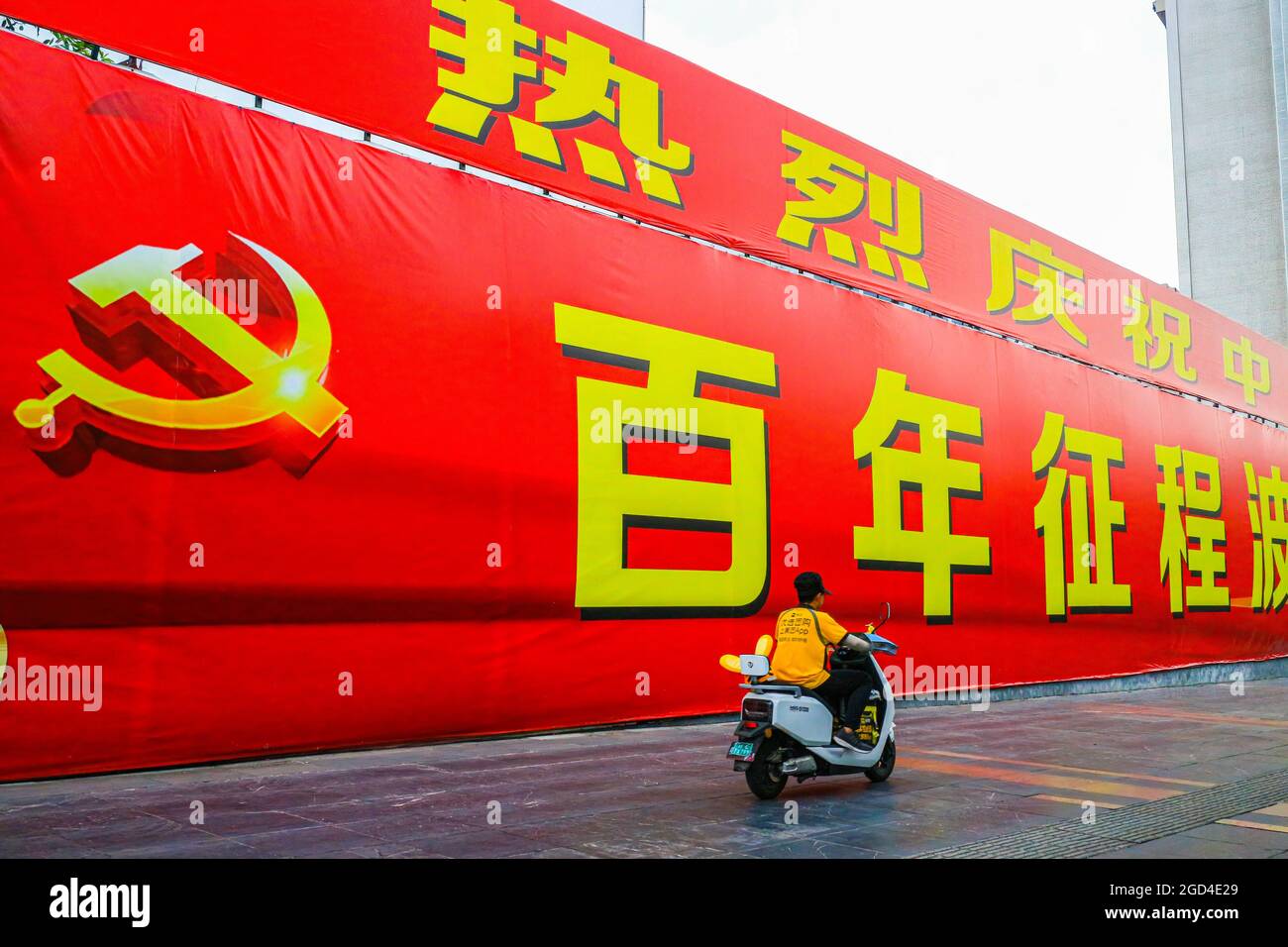 Un homme sur un scooter passe devant une immense bannière commémorant le 100e anniversaire de la fondation du Parti communiste chinois. Une bannière géante célébrant le 100e anniversaire de la fondation du Parti communiste de Chine est exposée sur l'avenue principale de Guilin, en Chine Banque D'Images