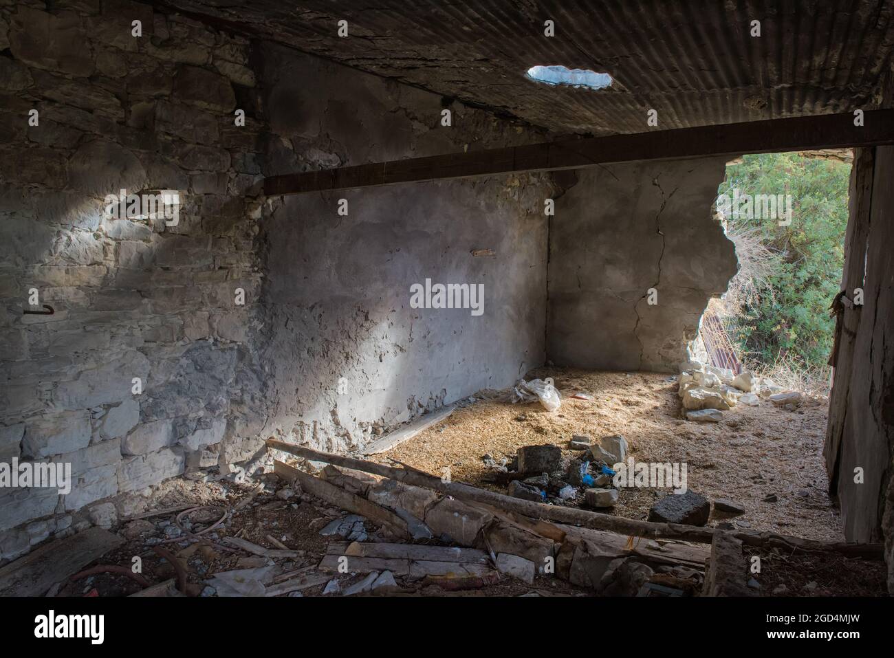 Ancienne grange abandonnée à l'intérieur d'un village avec des débris et de la lumière du soleil tombant à travers le mur et le toit cassés Banque D'Images