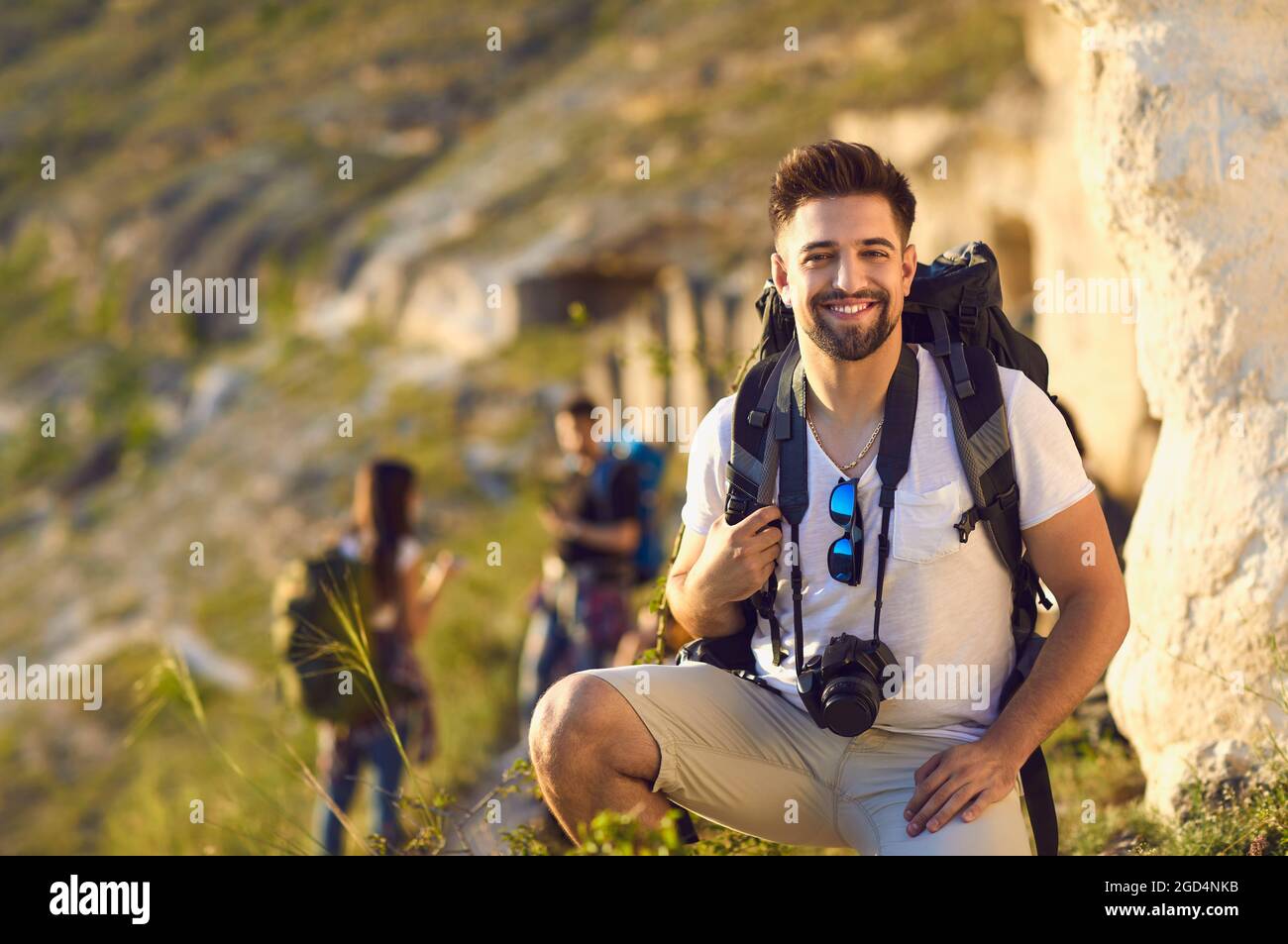 Portrait d'un jeune homme avec sac à dos et appareil photo en montagne. Touristes heureux et randonneurs flous lors d'une visite à pied en plein air Banque D'Images