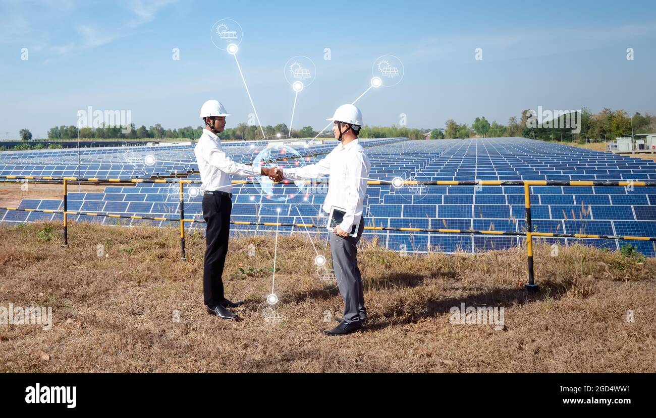 Les hommes d'affaires asiatiques se tiennent à la main avec le panneau solaire en arrière-plan. L'idée des investisseurs est de coopérer dans les affaires sur les énergies renouvelables à Banque D'Images