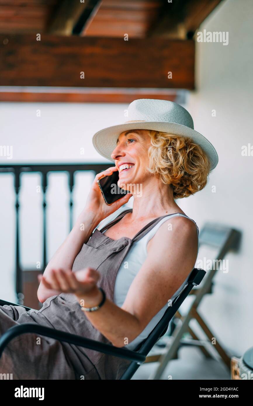 Femme blonde caucasienne adulte dans ses années 50 parlant sur un téléphone  mobile souriant et portant un chapeau et assis dans une posture détendue.  Concept de style de vie Photo Stock - Alamy