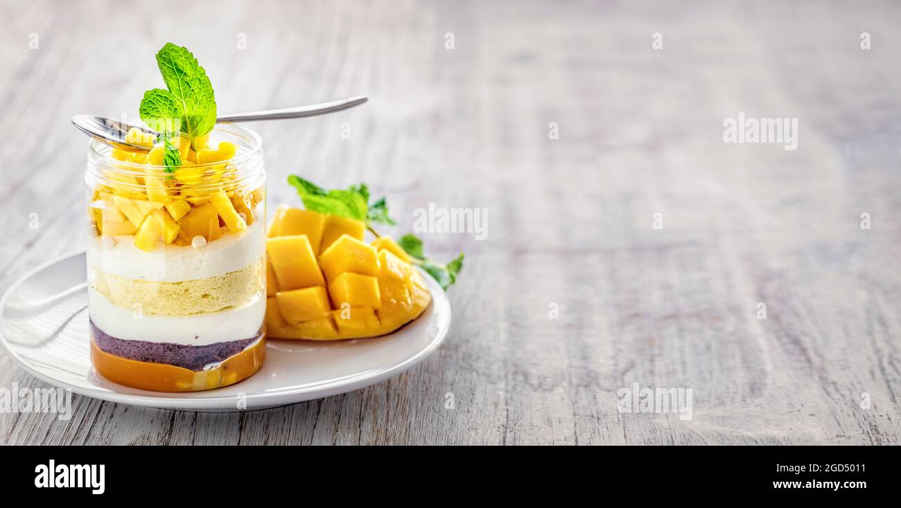 Dessert Mango maison, cheesecake, trifle, souris dans un pot en verre sur fond de bois clair, avec espace de copie Banque D'Images