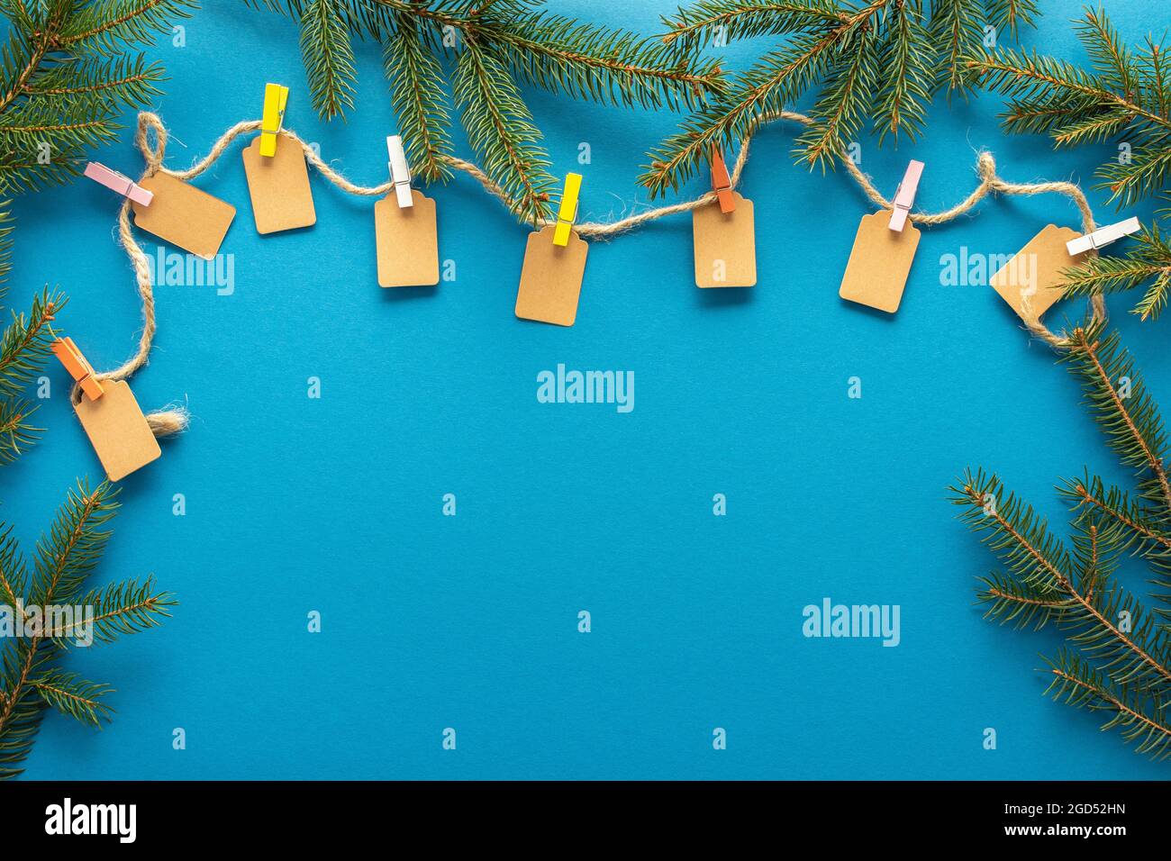 Étiquettes en papier attachées avec des épingles de couleur à la corde de jute, corde avec des étiquettes sur fond bleu avec des branches de sapin, fond de noël ou de nouvel an Banque D'Images