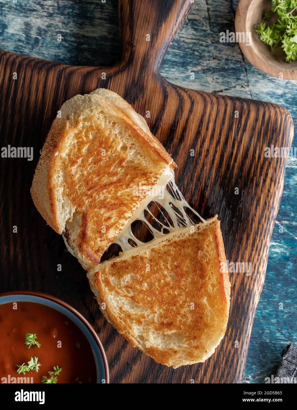Vue de haut en bas d'un sandwich au fromage grillé fait maison sur une planche de bois, servi avec une soupe de tomates. Banque D'Images