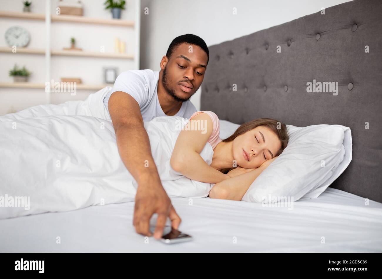 Jalousie, infidélité, problèmes de relation. Suspect mari noir vérifiant le téléphone portable de la femme dormant dans le lit à la maison. Contrôle Afro boyfriend Banque D'Images