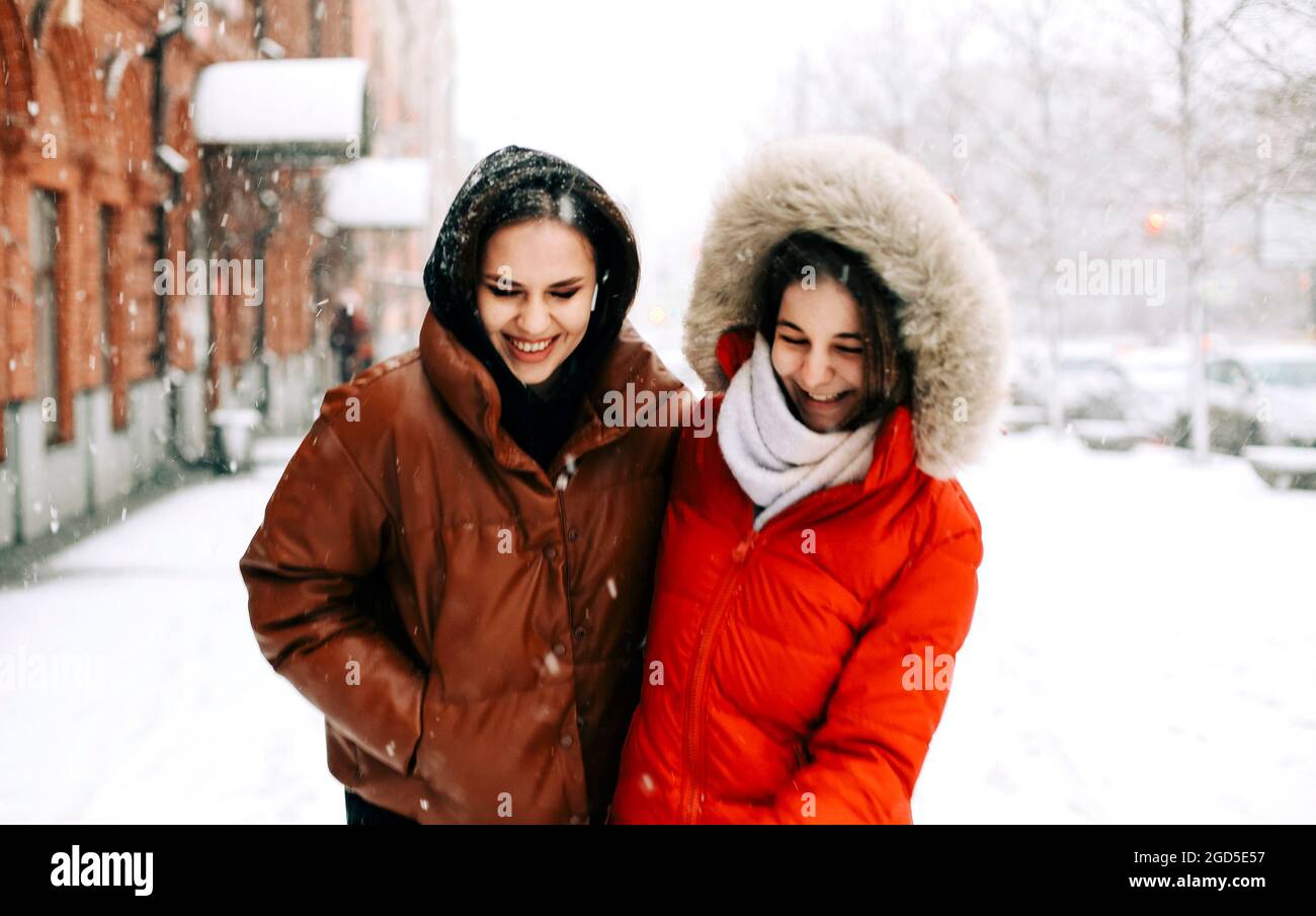 Deux amies joyeuses qui apprécient le temps de neige en plein air, les meilleures amies en hiver vêques en duvet vestes riant et s'amusant en marchant Banque D'Images