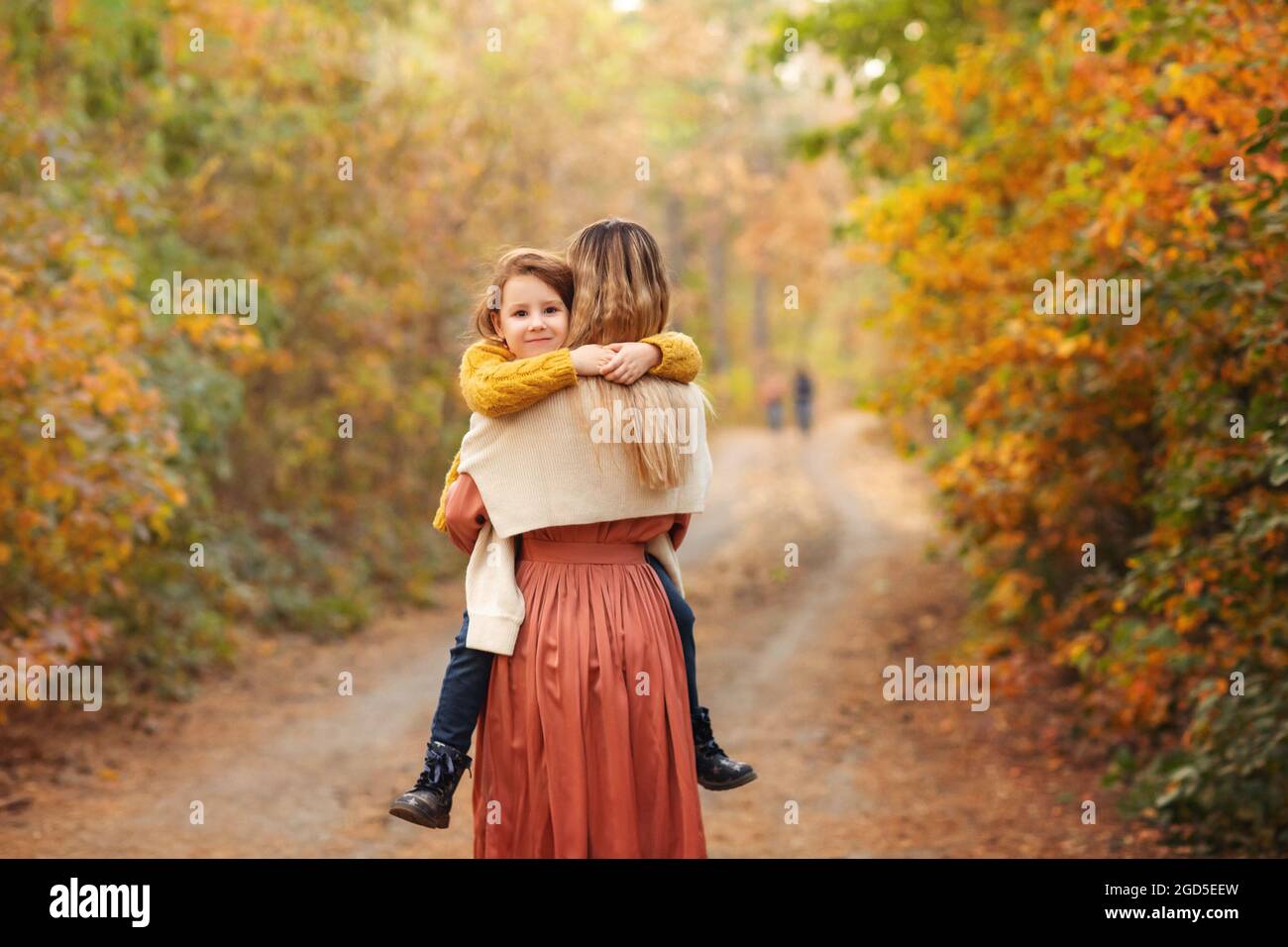 Jeune famille, mère et petit fils, sur la promenade dans la forêt d'automne, mère et enfant tenant les mains et marchant le long du chemin couvert de feuilles d'arbre jaune, spe Banque D'Images