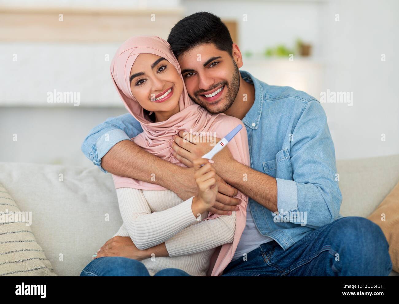 Couple Arabe Aimant Montrant Un Test De Grossesse Positif Assis Sur Un Canape A La Maison Et Souriant A La Camera Jeunes Conjoints En Attente De Bebe Nous Serons Parents Concep Photo