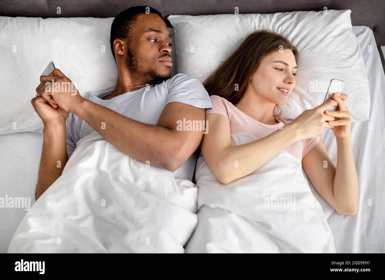Jeune couple interracial allongé dans le lit coincé dans les smartphones,  jouer à des jeux en ligne, parcourir les médias sociaux, vue de dessus.  Problèmes de relation, addic gadget Photo Stock -