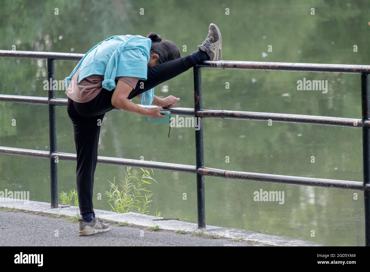 MULTITÂCHE. Une femme étire son hamstring et lit son téléphone cellulaire en même temps. À Kissena Park à Flushing, Queens, New York. Banque D'Images