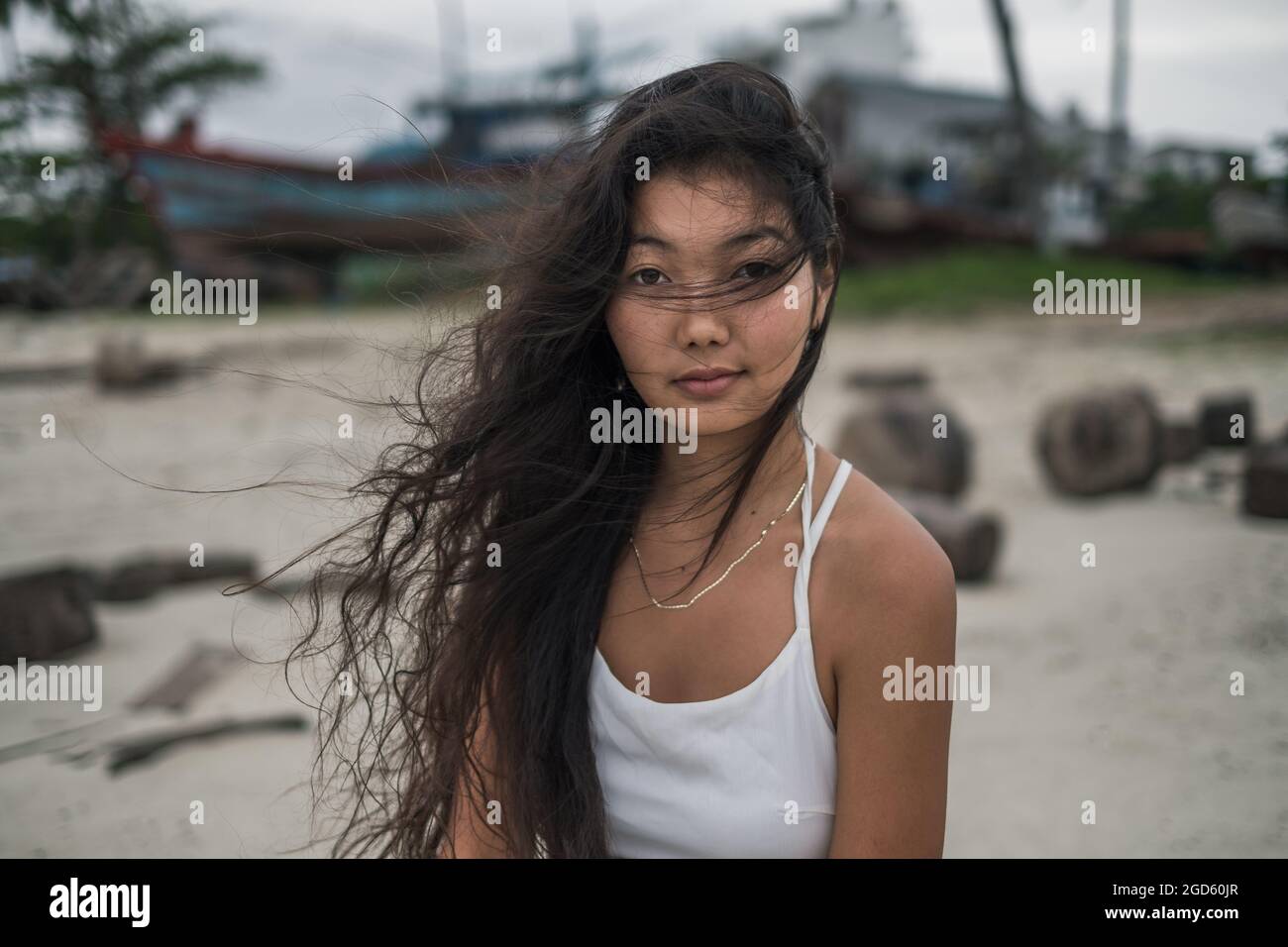 Charmante jeune femme asiatique en robe blanche assise sur la pierre et regardant de côté. Brunette cheveux longs bouclés. Photo romantique. Photo de haute qualité Banque D'Images