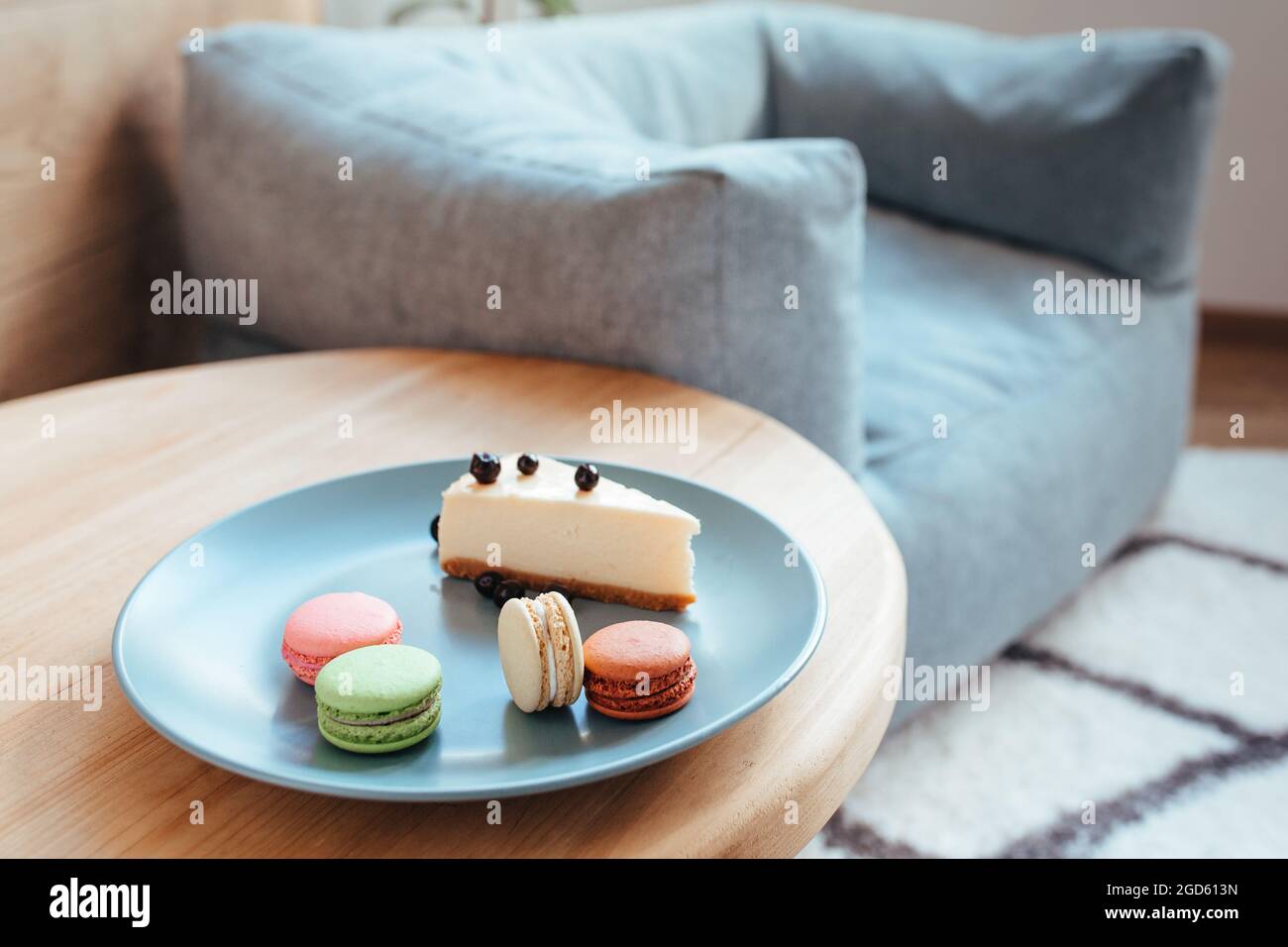 un gâteau au fromage avec cassis et macarons sur une assiette turquoise se trouve sur le bord de la table basse. Banque D'Images