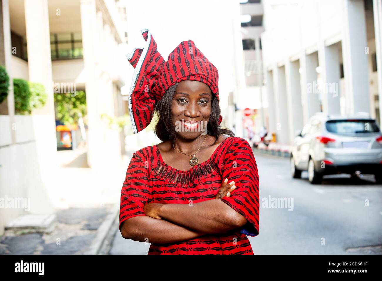 femme africaine mûre debout à l'extérieur tête attachée avec un morceau de tissu de longe regardant la caméra sourire. Banque D'Images