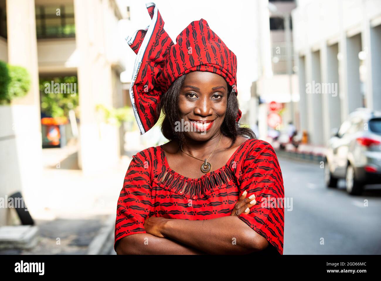 femme africaine mûre debout à l'extérieur tête attachée avec un morceau de tissu de longe regardant la caméra sourire. Banque D'Images