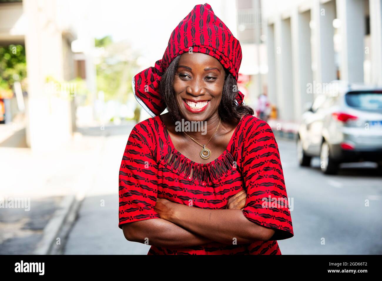 femme africaine mûre debout à l'extérieur tête attachée avec un morceau de tissu de longe regardant la caméra sourire. Banque D'Images