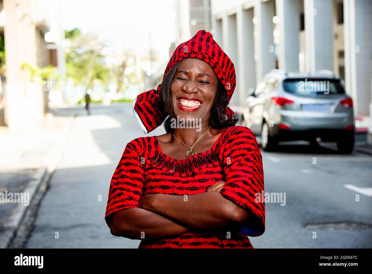 femme africaine mûre debout à l'extérieur tête attachée avec un morceau de tissu de longe regardant la caméra rire. Banque D'Images