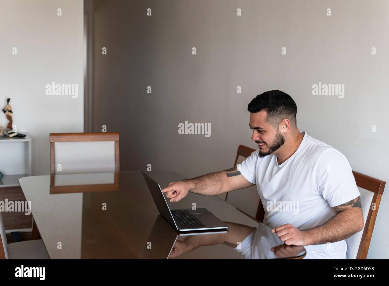Latino homme avec des tatouages pointant son doigt sur l'écran de l'ordinateur portable tout en souriant Banque D'Images